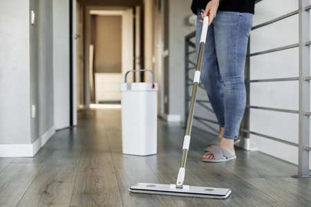 Woman mopping, wiping sleek hardwood floor in modern home setting. Housewife uses mop, bucket. Housekeeping, housework concept. Copy space. Sanitation, cleanliness, hygiene, cleanup, maintenanceの写真素材