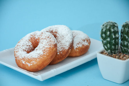 Pile of doughnuts in the powder give fine sugar, there are cactus tree accessories set in light blue
