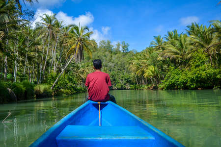A young man is at the end of the boat enjoying the atmosphere and the beauty of the Maron River in Pacitan Indonesia, he is happy.の写真素材