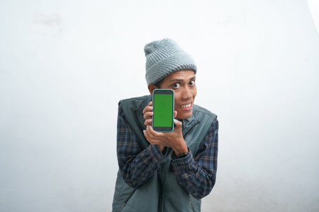 Asian young man wearing dark blue vest and beanie, isolated on white background giving shocked...