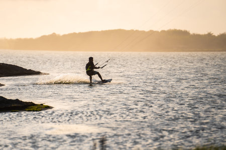 kitesurfing. A surfer rides on a beautiful backdrop of bridges and coastline at sunset and performs all kinds of stunts. : Yogyakarta, Indonesia - 26 August 2023のeditorial素材