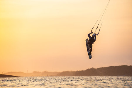 kitesurfing. A surfer rides on a beautiful backdrop of bridges and coastline at sunset and performs...
