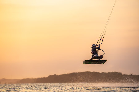 kitesurfing. A surfer rides on a beautiful backdrop of bridges and coastline at sunset and performs all kinds of stunts. : Yogyakarta, Indonesia - 26 August 2023のeditorial素材