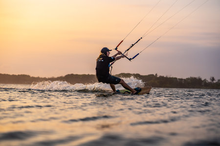 kitesurfing. A surfer rides on a beautiful backdrop of bridges and coastline at sunset and performs all kinds of stunts. : Yogyakarta, Indonesia - 26 August 2023のeditorial素材