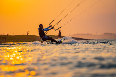 kitesurfing. A surfer rides on a beautiful backdrop of bridges and coastline at sunset and performs all kinds of stunts. : Yogyakarta, Indonesia - 26 August 2023のeditorial素材