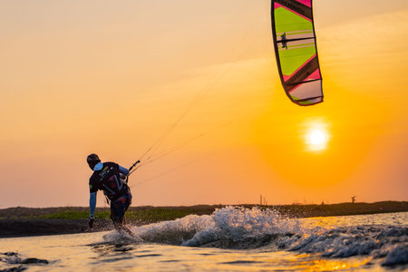 kitesurfing. A surfer rides on a beautiful backdrop of bridges and coastline at sunset and performs all kinds of stunts. : Yogyakarta, Indonesia - 26 August 2023のeditorial素材
