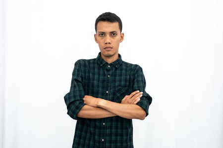 Asian man wearing a casual green checkered shirt poses with his arms folded on his stomach. business photo concept, cool student. Isolated white background.の写真素材
