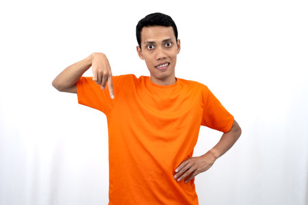 Portrait of a young Asian man wearing an orange t-shirt pointing down copy space for promotional space. isolated on white background.の写真素材