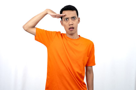 Portrait of a young Asian man wearing an orange t-shirt looking surprised, shocked and shocked....