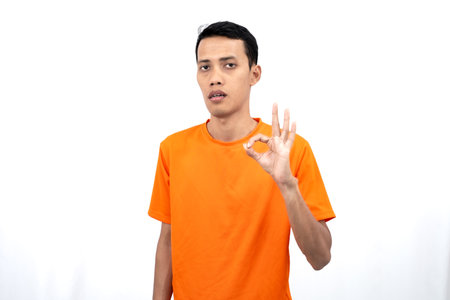 Portrait of a young Asian man wearing an orange t-shirt giving a thumbs up, okay, agree sign. isolated on white background.の写真素材