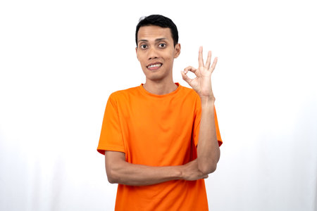 Portrait of a young Asian man wearing an orange t-shirt giving a thumbs up, okay, agree sign. isolated on white background.の写真素材