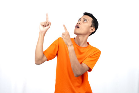 Portrait of a young Asian man wearing an orange t-shirt pointing upwards at copy space for promotional space. isolated on white background.の写真素材