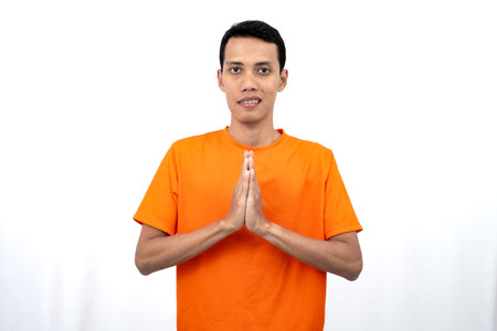 Portrait of a young Asian man wearing an orange t-shirt posing and giving a warm greeting. Isolated on white background.の写真素材