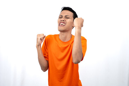 Portrait of a young Asian man wearing an orange t-shirt with a happy expression, surprised to get good news. Isolated on white background.の写真素材
