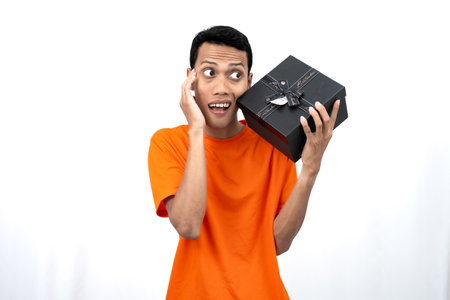 Portrait of a young Asian man wearing an orange t-shirt with a happy expression, surprised to get a gift. Isolated on white background.の写真素材