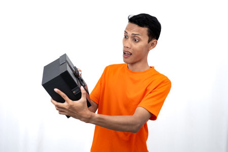 Portrait of a young Asian man wearing an orange t-shirt with a happy expression, surprised to get a gift. Isolated on white background.の写真素材