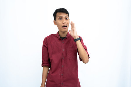 Asian man, wearing red casual shirt, shouting with hand in mouth, isolated on white background.の写真素材