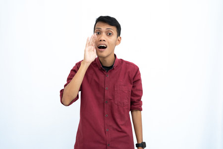 Asian man, wearing red casual shirt, shouting with hand in mouth, isolated on white background.の写真素材