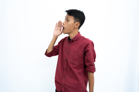 Asian man, businessman or student concept wearing red casual shirt, shouting with hand in mouth, giving information or whispering, isolated on white background.の写真素材