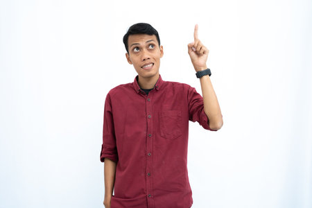 Asian man, businessman or student concept wearing red casual shirt pointing up at the copy space with a happy or surprised look on his face. Isolated white background.の写真素材