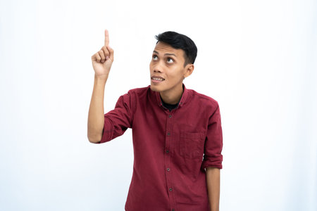 Asian man, businessman or student concept wearing red casual shirt pointing up at the copy space with a happy or surprised look on his face. Isolated white background.の写真素材