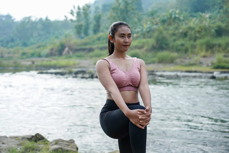 A slender Asian girl with brown skin in sportswear doing muscle warm-up movements in the open air on...