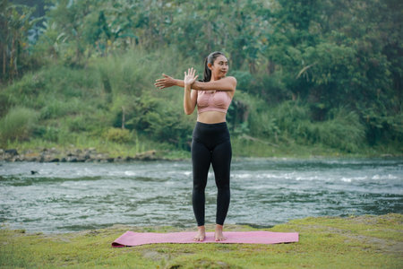 A slender Asian girl with brown skin in sportswear is doing shoulder muscle stretching movements in...