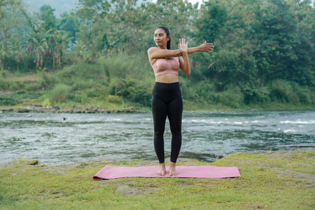 A slender Asian girl with brown skin in sportswear is doing shoulder muscle stretching movements in...