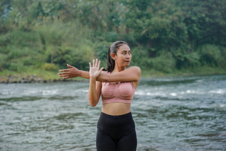 A slender Asian girl with brown skin in sportswear is doing shoulder muscle stretching movements in...
