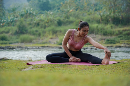 A slender Asian girl with brown skin in sportswear is doing stretching movements of her hamstrings...