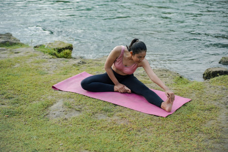 A slender Asian girl with brown skin in sportswear is doing stretching movements of her hamstrings...