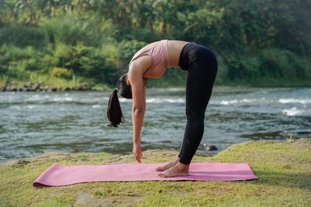 A slender, tanned Asian girl in sportswear performs the inchworm stretch outdoors on a beautiful...