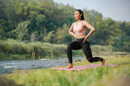 A slender, tanned girl in sportswear performs lunge stretching exercises outdoors in a beautiful...