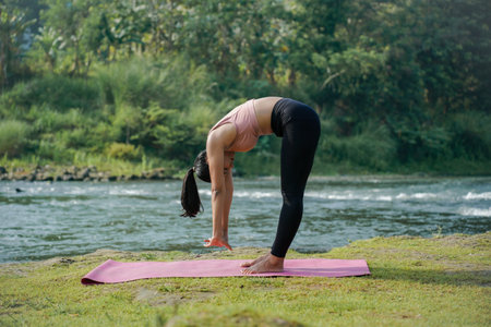 A slender, tanned Asian girl in sportswear performs the inchworm stretch outdoors on a beautiful...