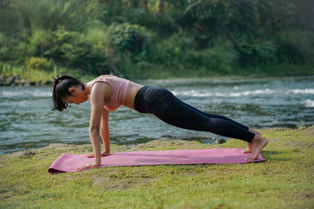 A slender, tanned Asian girl in sportswear performs the inchworm stretch outdoors on a beautiful...