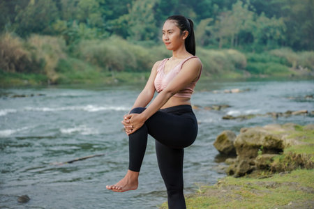 A slender Asian girl with brown skin in sportswear doing muscle warm-up movements in the open air on...
