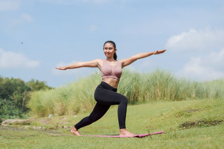 Mental and physical health. A woman in sportswear does yoga by a calm river in the morning. The woman stands in a warrior pose with her arms outstretched.の写真素材
