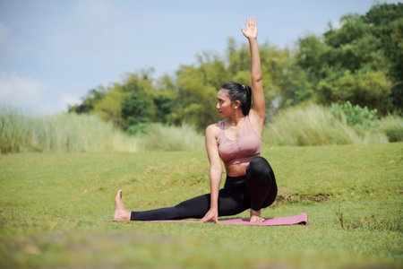 Mental and physical health. A slender, tanned girl in sportswear does yoga by a calm river in the morning. The woman stands in a warrior pose with her arms outstretched.の写真素材