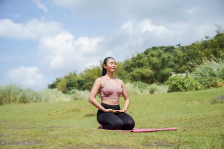 Mental and physical health. A slender, tanned Asian woman in sportswear performs yoga in a peaceful, natural setting early in the morning. The woman is in Virasana, or Hero Pose.の写真素材