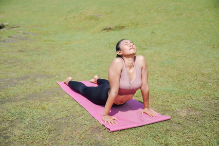 Mental and physical health. A slender, tanned Asian woman in sportswear performs yoga outdoors in a...