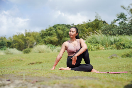 Mental and physical health. A slender, tanned Asian woman in sportswear performs yoga outdoors in a...