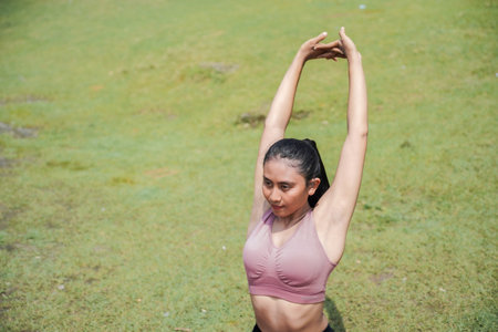 A slender, tanned Asian girl in sportswear performs yoga poses outdoors in a beautiful riverside setting in the morning. The theme is meditation on health, mental, and physical well-being.の写真素材