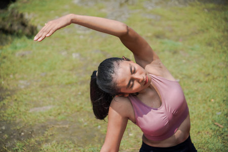 A slender, tanned Asian girl in sportswear performs yoga poses outdoors in a beautiful riverside...