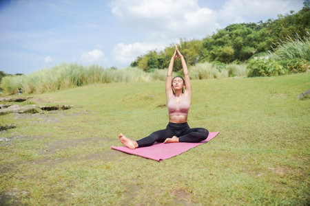 A slender, tanned Asian girl in sportswear performs yoga poses outdoors in a beautiful riverside...