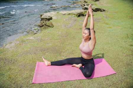 A slender, tanned Asian girl in sportswear performs yoga poses outdoors in a beautiful riverside...