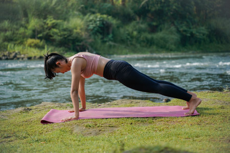 A slender, tanned Asian girl in sportswear performs the inchworm stretch outdoors on a beautiful...