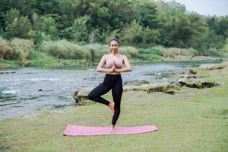 Mental and physical health. A slender, tanned Asian woman in sportswear performs yoga outdoors in a...