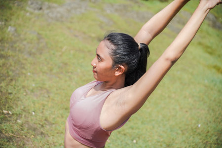 A slender, tanned Asian girl in sportswear performs yoga poses outdoors in a beautiful riverside setting in the morning. The theme is meditation on health, mental, and physical well-being.の写真素材