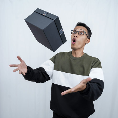 An Asian young man with glasses wearing a sweater with a surprised happy expression getting a...
