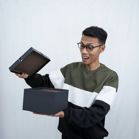 An Asian young man with glasses wearing a sweater with a surprised happy expression getting a...